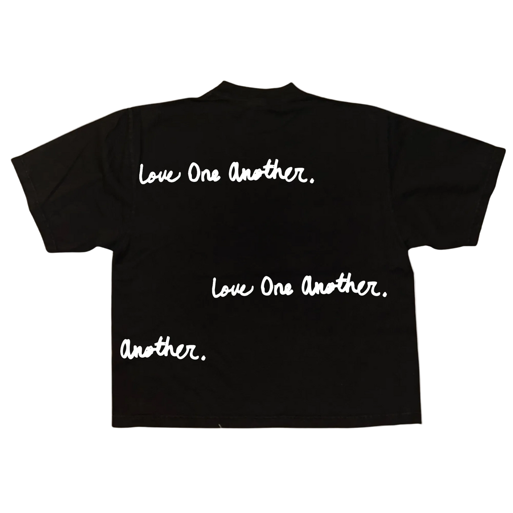 A black short-sleeve t-shirt shown from the back, featuring the phrase 'Love One Another.' printed in white script across the upper back, with additional text 'Love One Another.