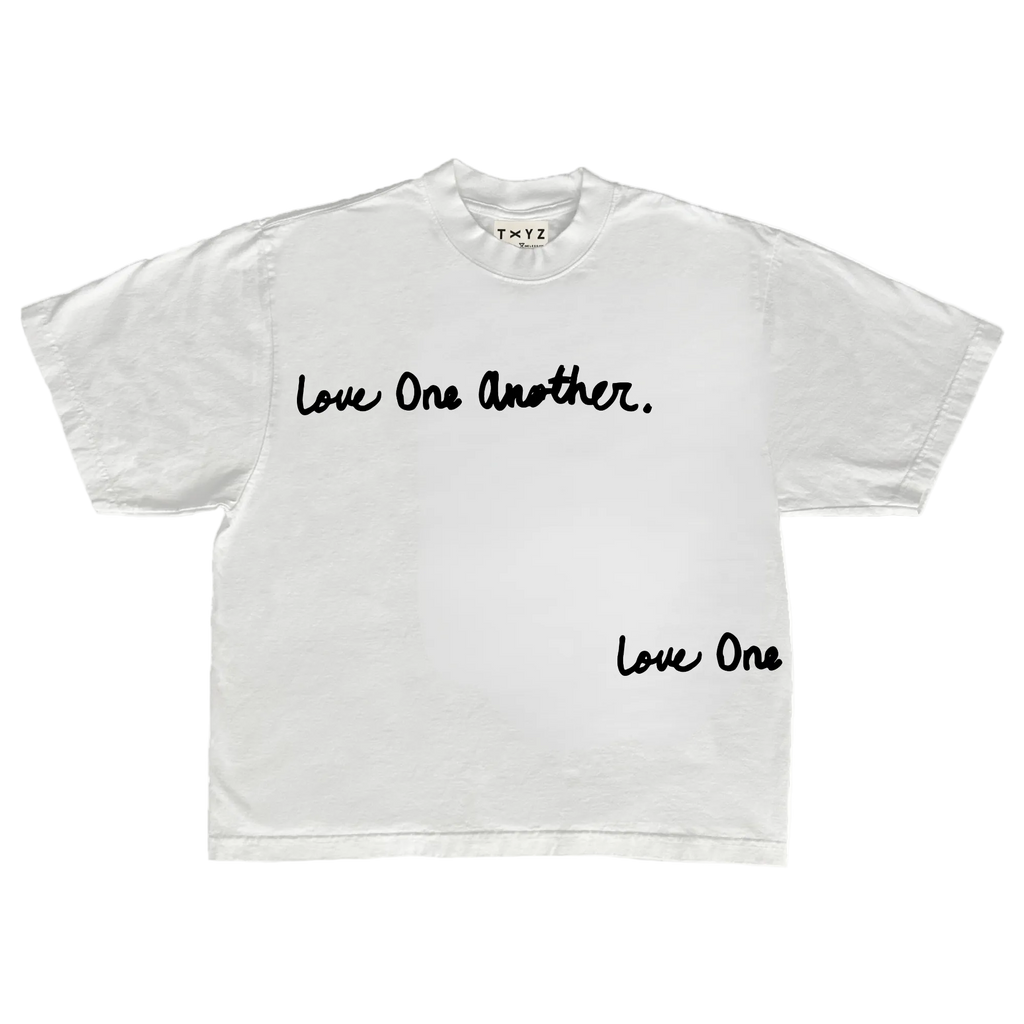 A white short-sleeve crewneck t-shirt with black script text reading 'Love One Another.' across the chest and 'Love One' printed near the lower right hem, shown flat against a white background.